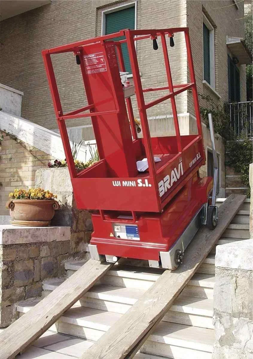 Arbeitsbühne auf Rollen, die über zwei an einer Treppe angelegte Holzbretter hochgefahren wird.
