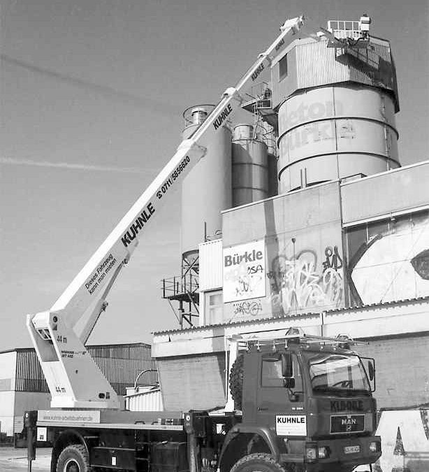 Historisches Schwarzweißfoto: Arbeitsbühne ausgefahren, an Gebäude und hohem Turm im Hintergrund.