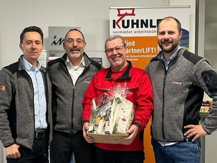 4 Männer, einer hält Geschenkkorb, hinten Kuhnle Banner.