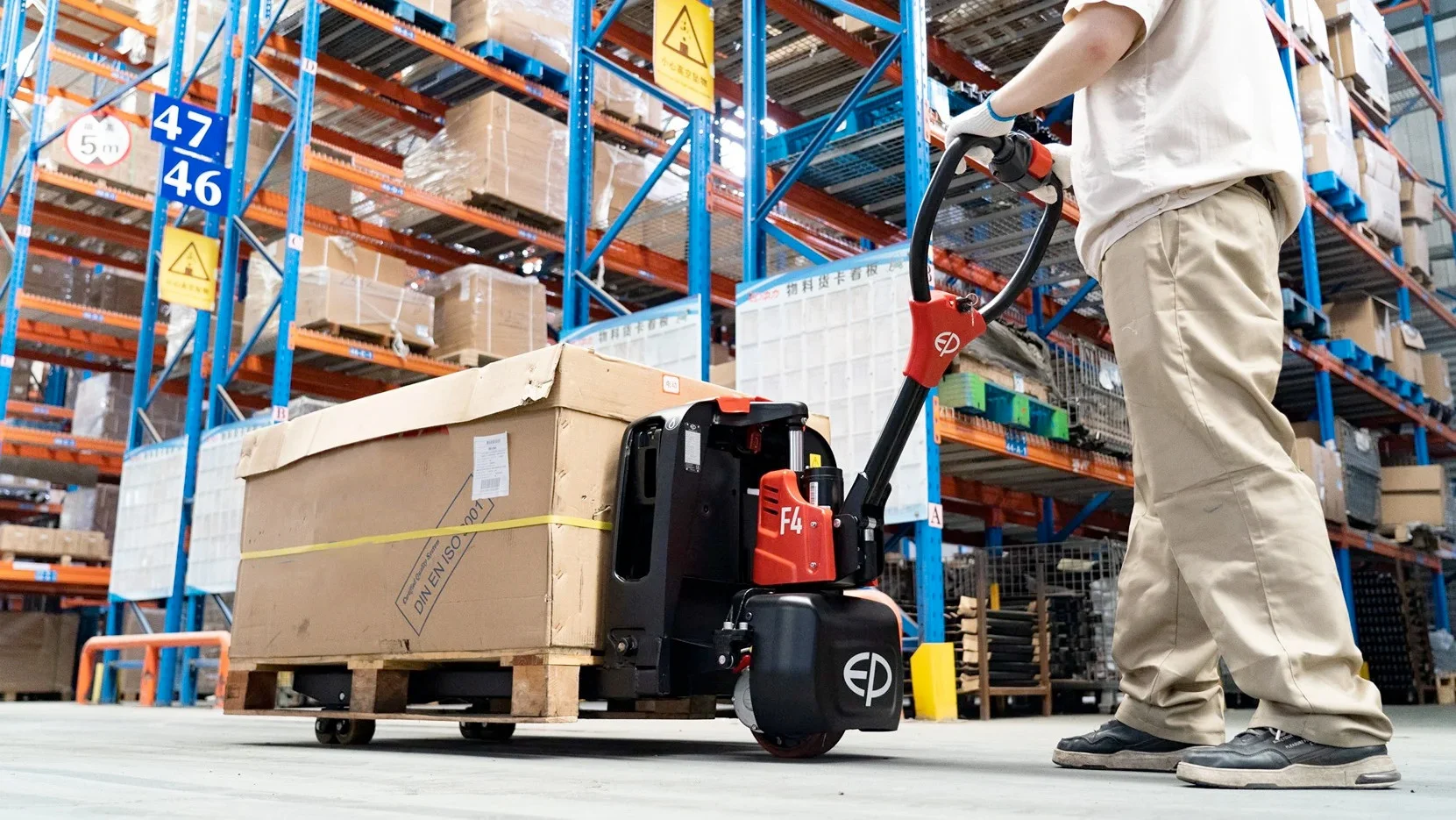 Person schiebt geladenen Hubwagen mit Kartons, im Hintergrund Lager mit hohen blauen Regalen voller Kartons.
