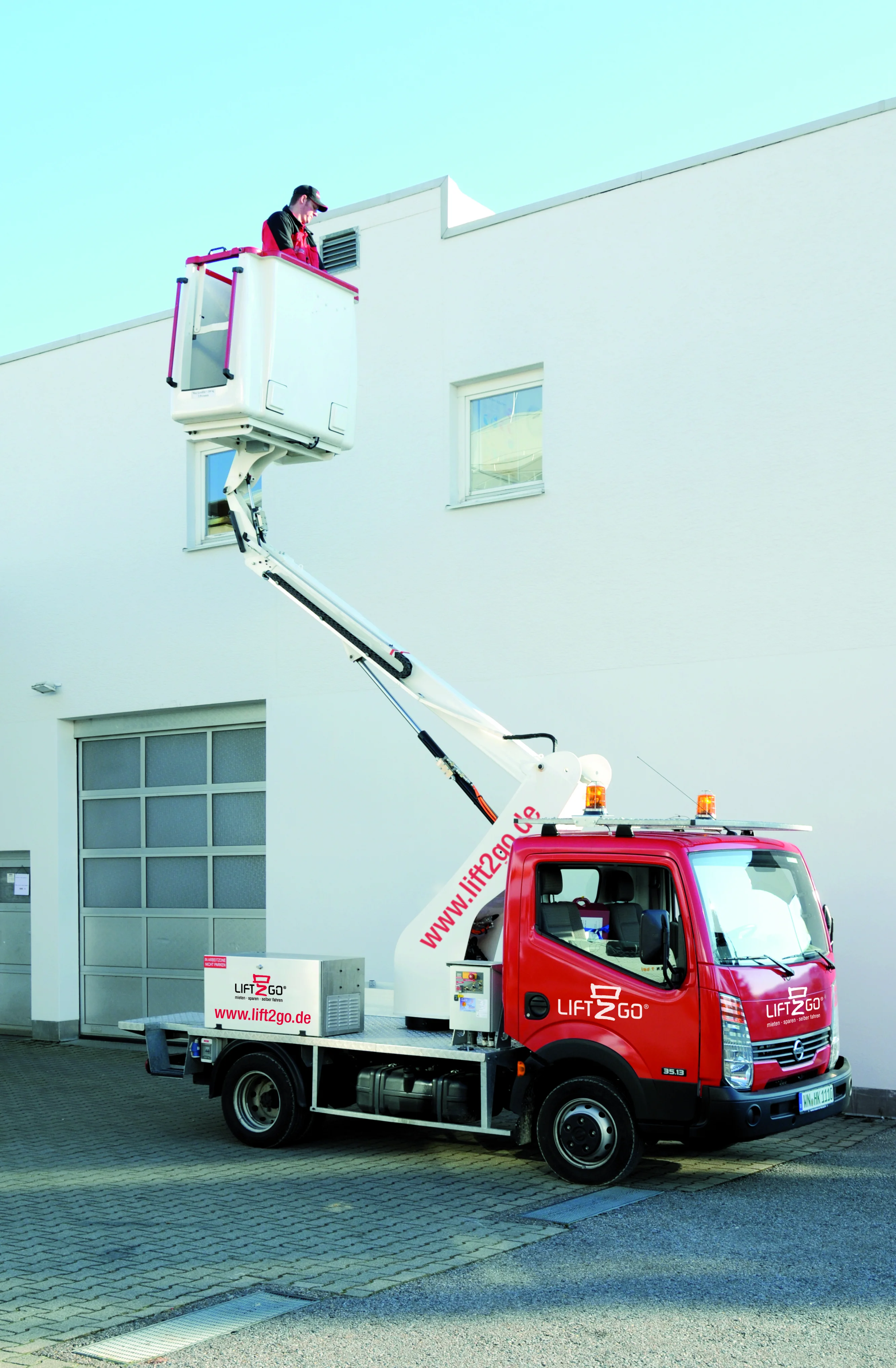 Ausgefahrene Arbeitsbühne vor weißem Gebäude, eine Person darauf.