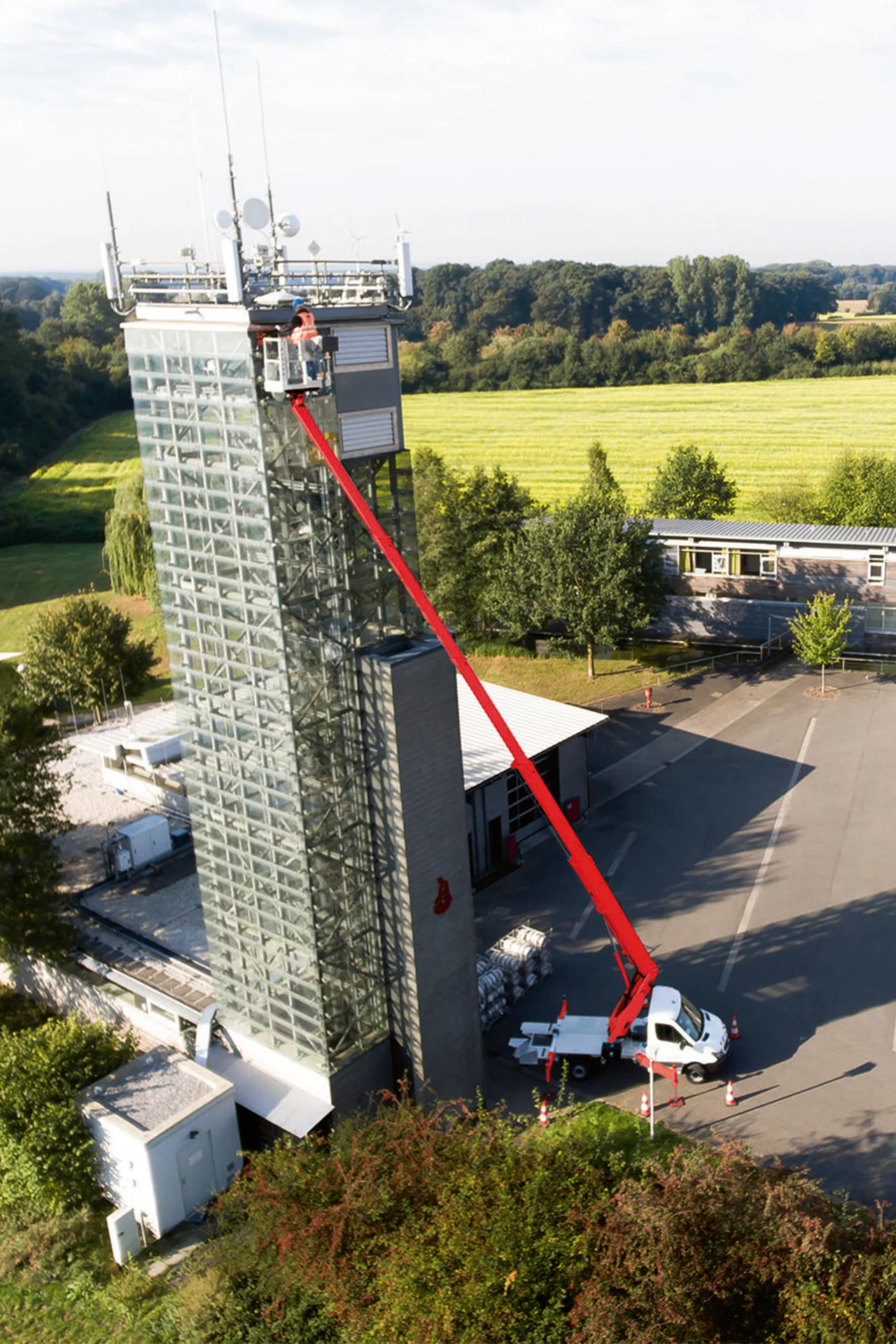 Hochhaus links, Arbeitsbühne ausgefahren, rechts Hof, dahinter Feld und Wald sichtbar.
