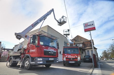 Gebäude vor blauem Wolkenhimmel, an zwei Seiten jeweils eine Arbeitsbühne.