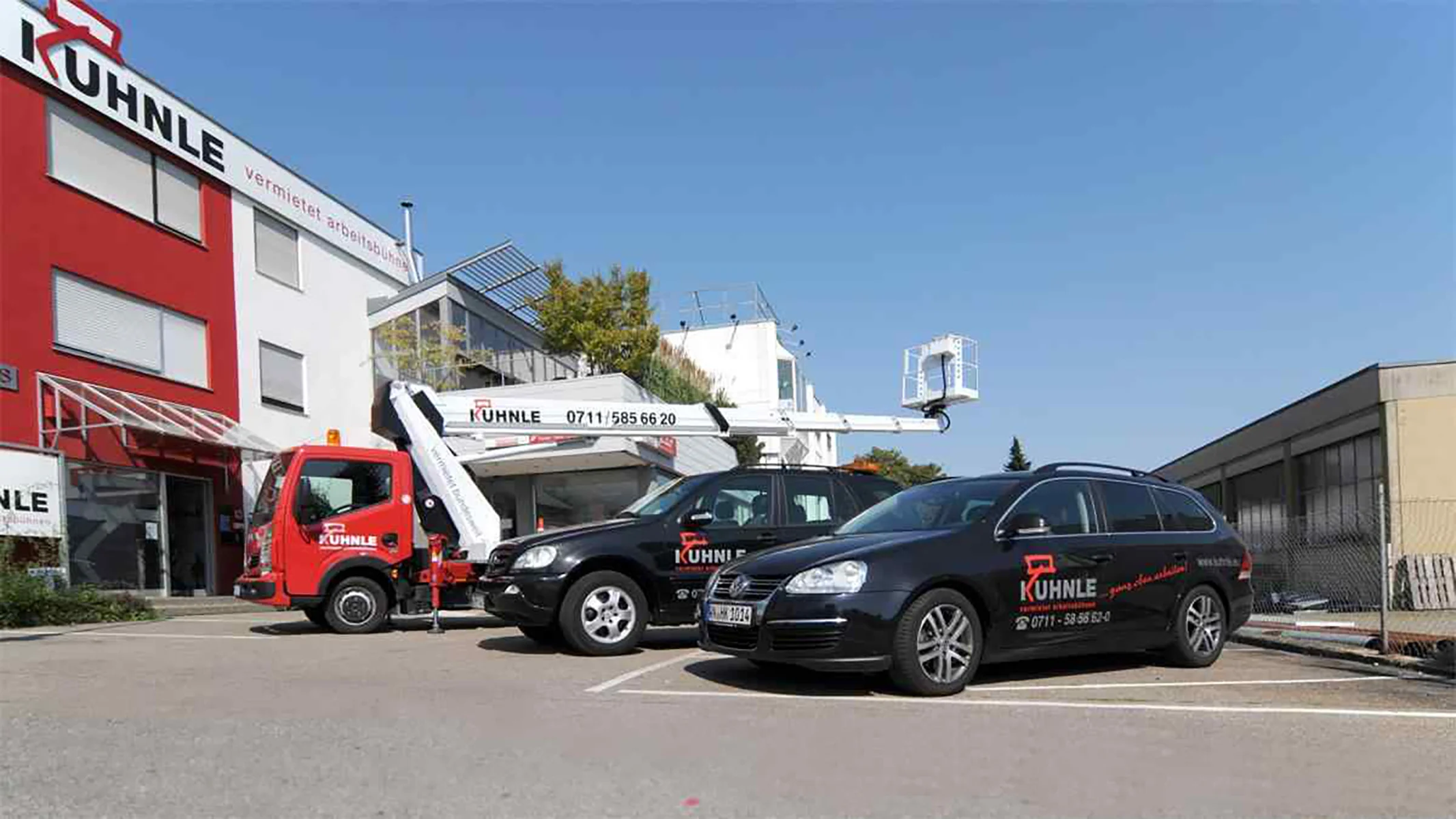 Kuhnle Gebäude, davor eine Arbeitsbühne und zwei schwarze Autos geparkt.