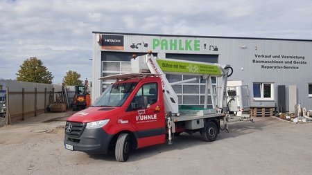 Weg und Gebäude, davor rote Arbeitsbühne.