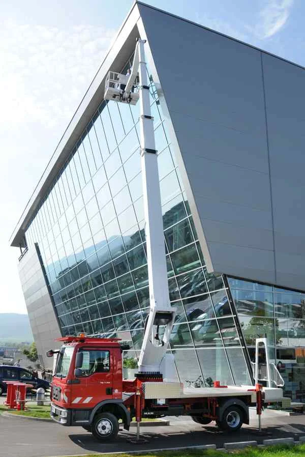 Ausgefahrene Arbeitsbühne vor Gebäude mit Glasfront.