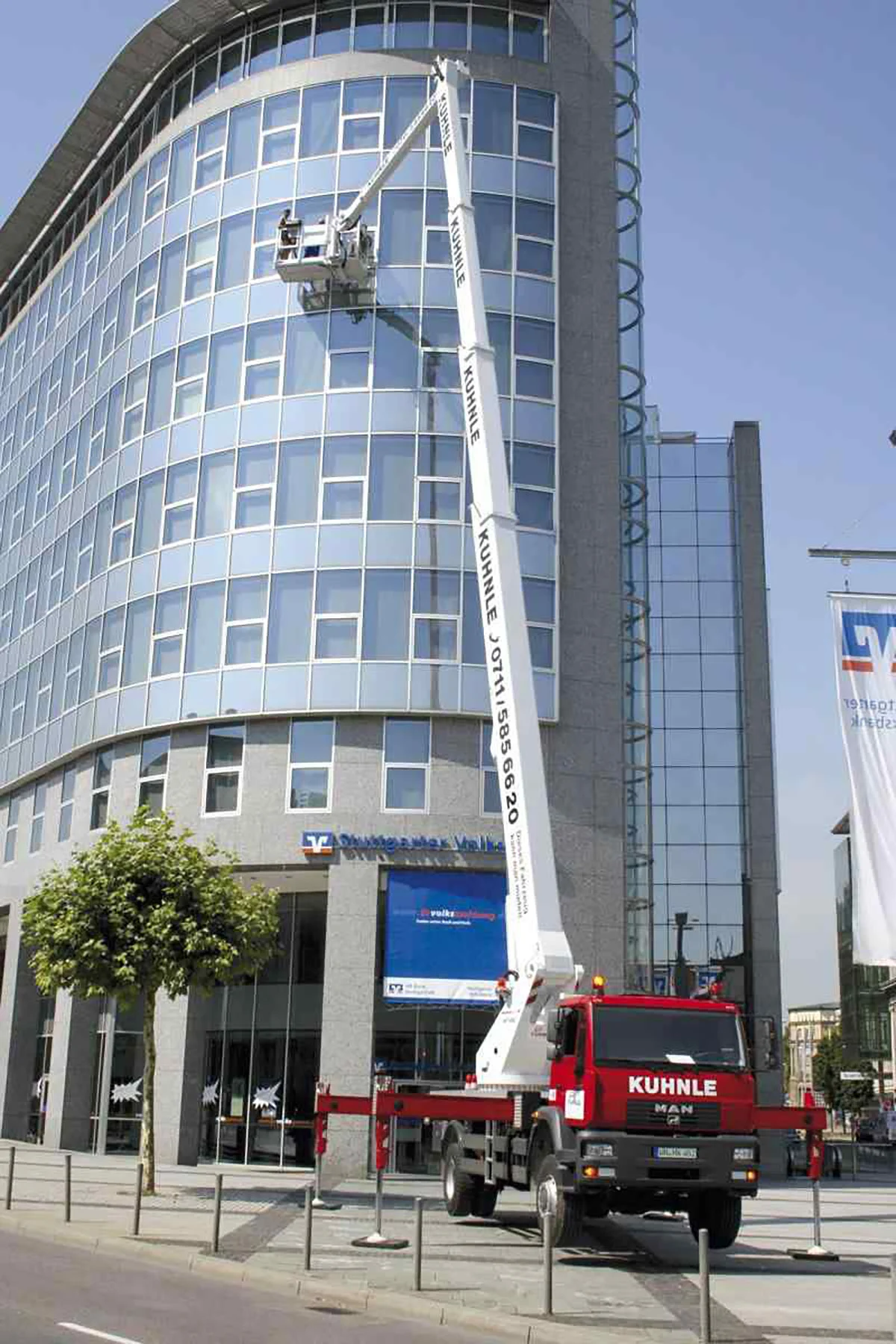 Gehweg vor Gebäude mit Fensterfront, darauf ausgefahrene Arbeitsbühne.
